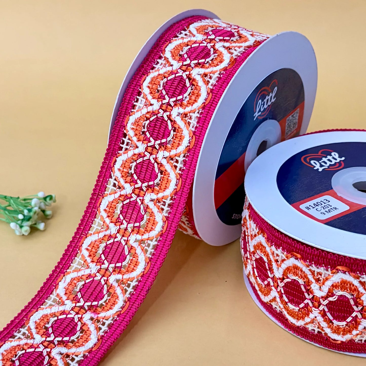 two spools of decorative ribbon with a pink, orange, and white pattern on a beige background.