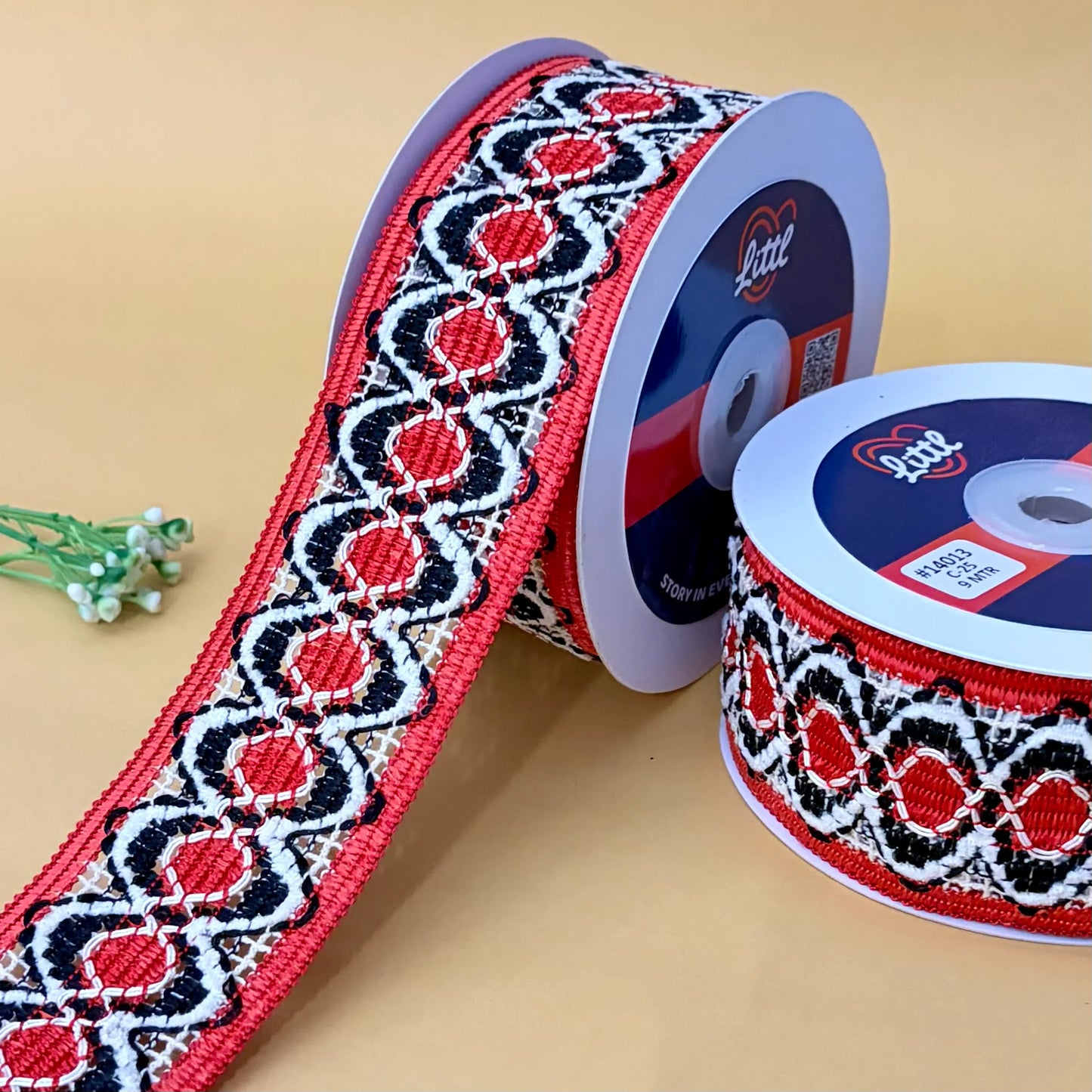 two spools of ribbon with a red, black, and white pattern on a beige background.