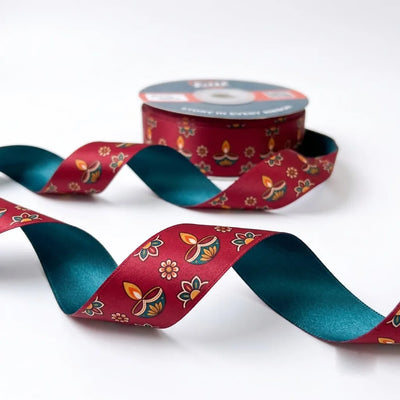 Close-up of Diya Glow ribbon: glowing diyas and flowers printed on festive red satin