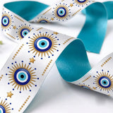 Close-up of Nazar Sun ribbon: blue evil eyes with gold sunburst rays printed on white satin, turquoise back