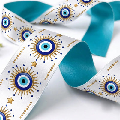 Close-up of Nazar Sun ribbon: blue evil eyes with gold sunburst rays printed on white satin, turquoise back