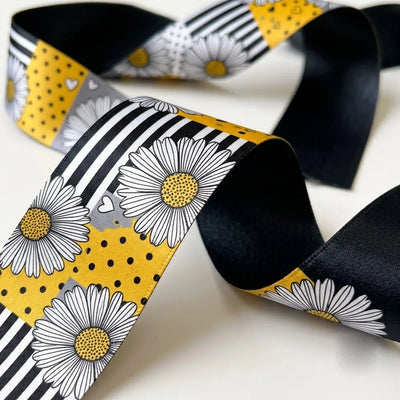 Close-up of Daisy Patchwork ribbon: white daisies on a patchwork of stripes and polka dots printed on black, grey and yellow satin, black back