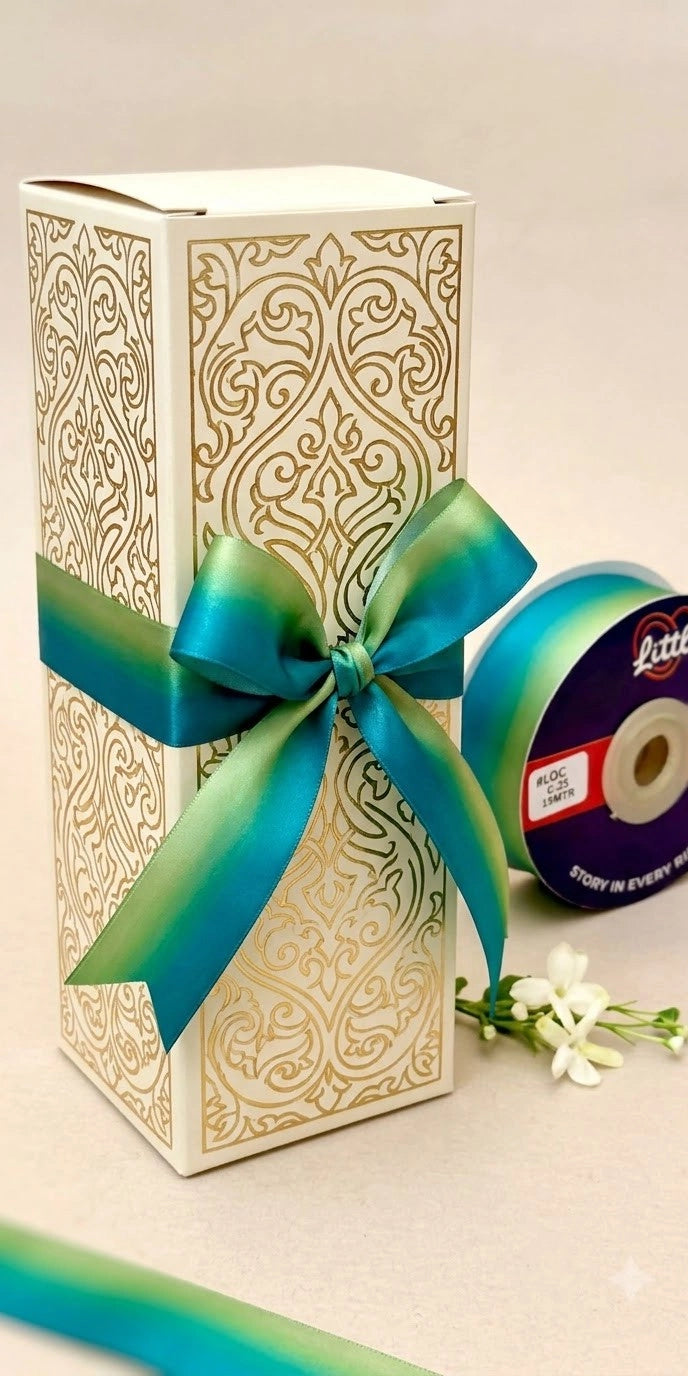 Ivory and gold gift box tied with a teal-to-green ombré satin ribbon bow, next to a Littl ribbon spool